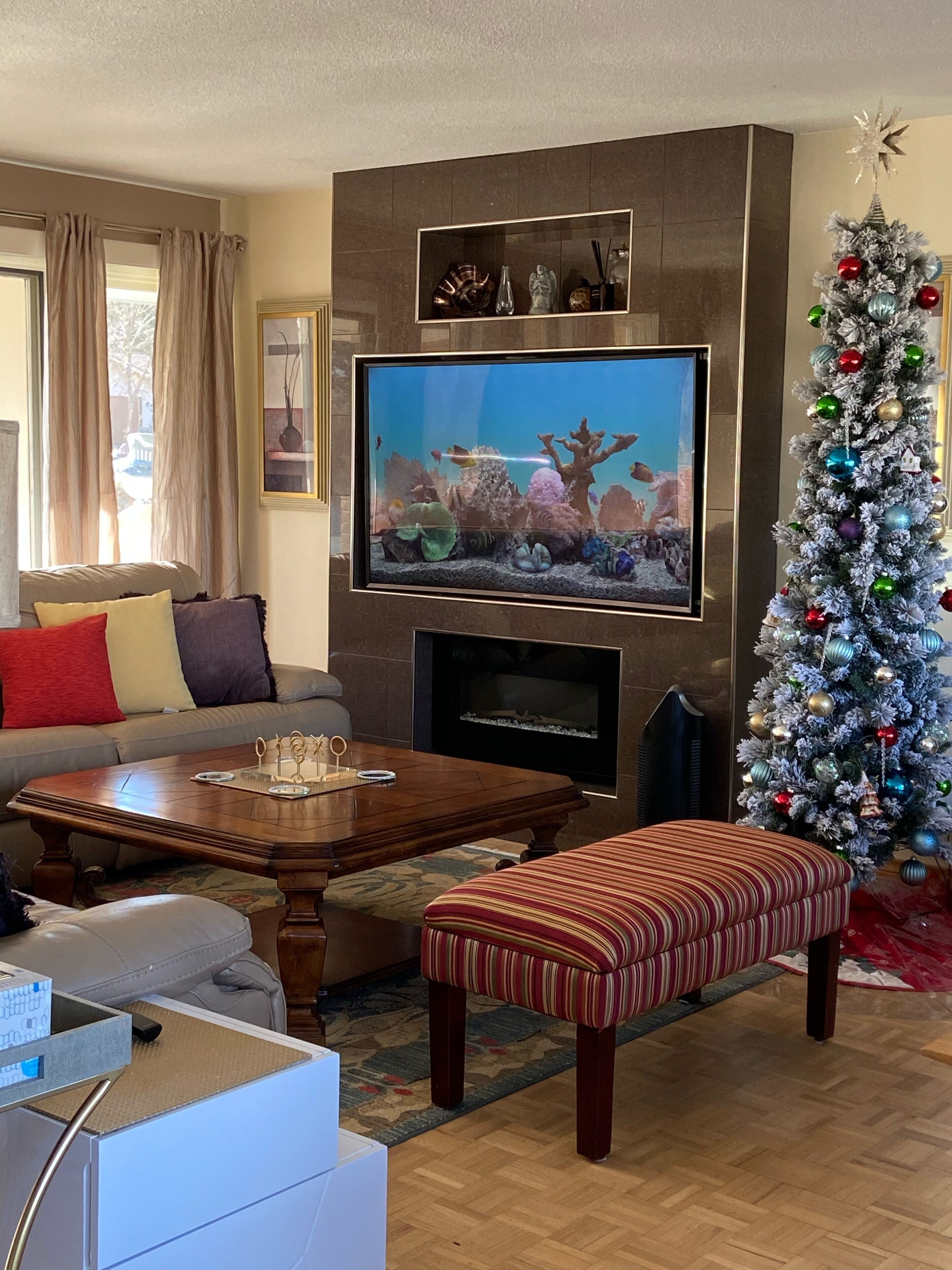 Een woonkamer met een grote televisie, een open haard, een kerstboom en een bank.