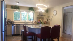 Et moderne køkken med en central ø, rustfrie hårde hvidevarer og røde barstole.