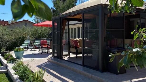 En moderne udendørs terrasse med glasafskærmning, havemøbler og en rød parasol.