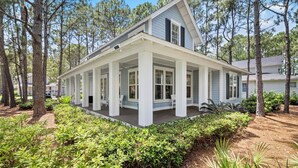 A two-story house with a covered porch, surrounded by trees and greenery.