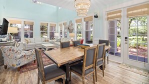A spacious living room with a wooden dining table, comfortable seating, and large windows offering views of the outdoors.