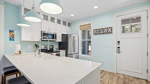 A modern kitchen with white cabinets, a large island, stainless steel appliances, and a 'RELAX' sign on the door.
