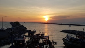 A harbor at sunset with boats docked, a pier extending into the water, and a small building on the left.