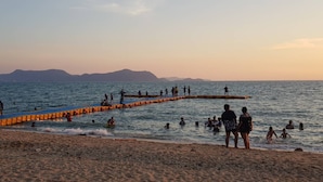 A beach with people swimming and walking along a wooden jetty.