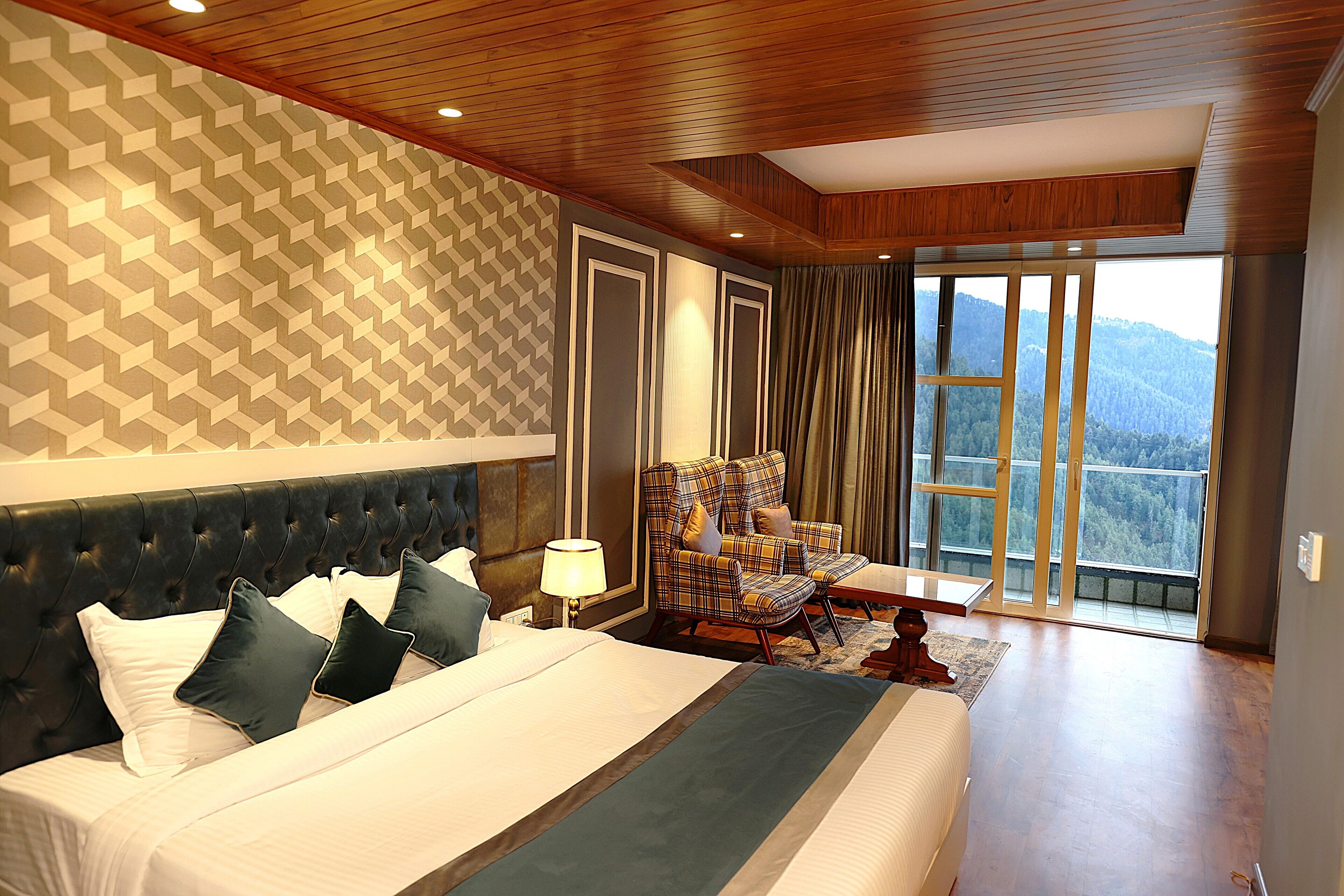 A hotel room with a large bed, a chair, a table, and a view of the mountains.