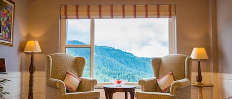 Une pièce avec deux fauteuils placés face à une grande fenêtre donnant sur un paysage de montagne. Une petite table avec un objet décoratif se trouve devant la fenêtre.