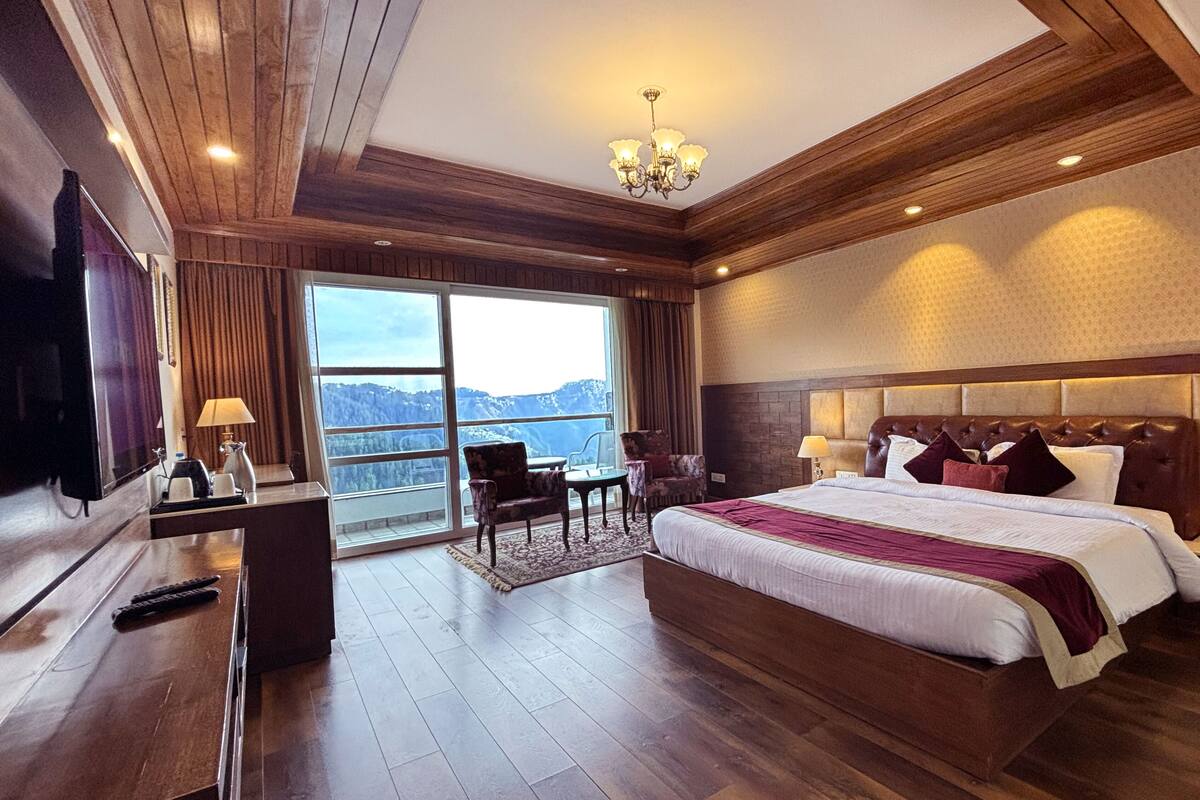 Amplia habitación de hotel con una cama grande, un escritorio con silla, televisión y vistas a las montañas.