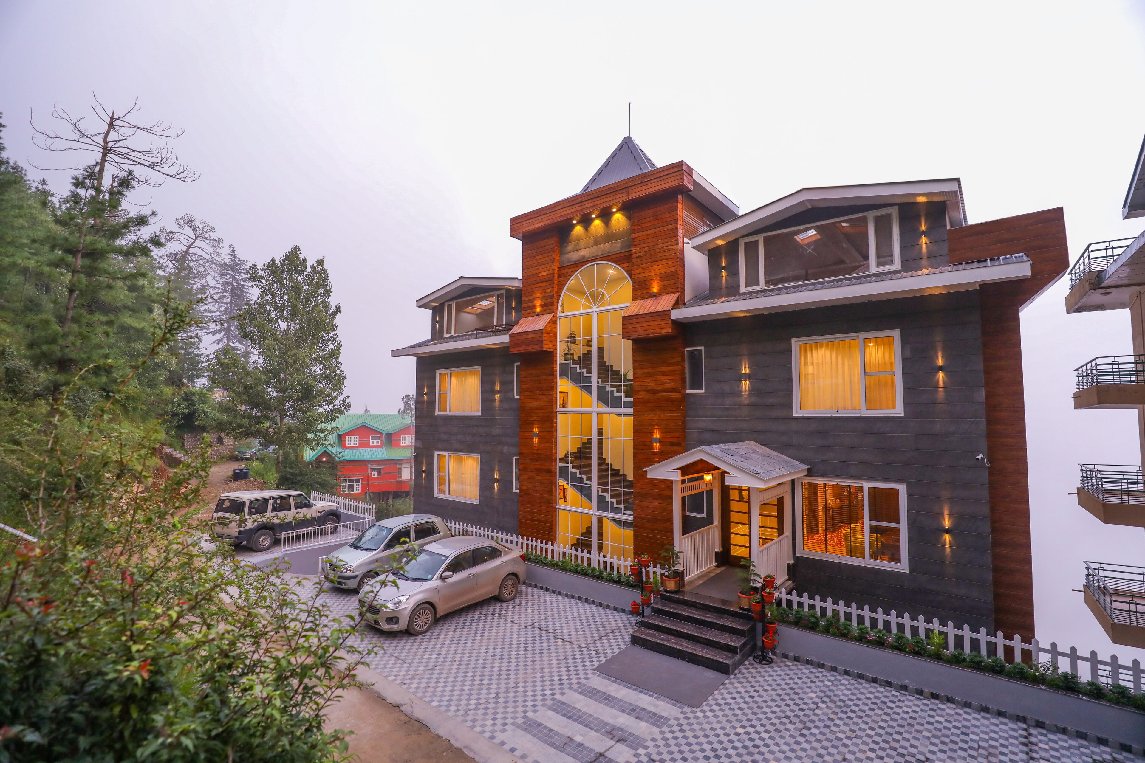 A modern multi-story building with a prominent staircase, a fenced driveway, and parked cars.