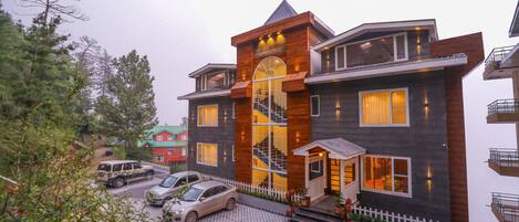 A modern multi-story building with a prominent staircase, a fenced driveway, and parked cars.
