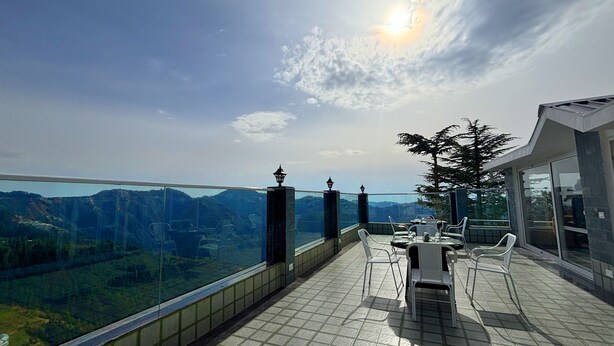 A terrace with a panoramic view of mountains, a dining table with chairs, and a glass railing. - The Retreat Mashobra, Shimla (Shimla)