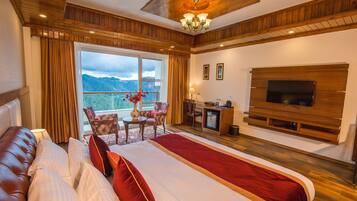 A spacious bedroom with a large bed, a TV mounted on the wall, a desk with a chair, and a view of the outdoors.