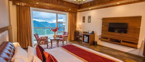 Un dormitorio espacioso con una cama grande, un televisor montado en la pared, un escritorio con silla y vistas al exterior.