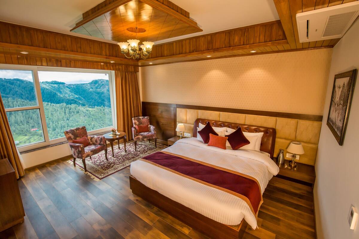 Un dormitorio espacioso con una cama grande, piso de madera, vistas al exterior y un candelabro.