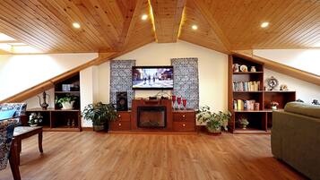 A cozy living room with a wooden ceiling, a fireplace, a television, and a bookshelf.
