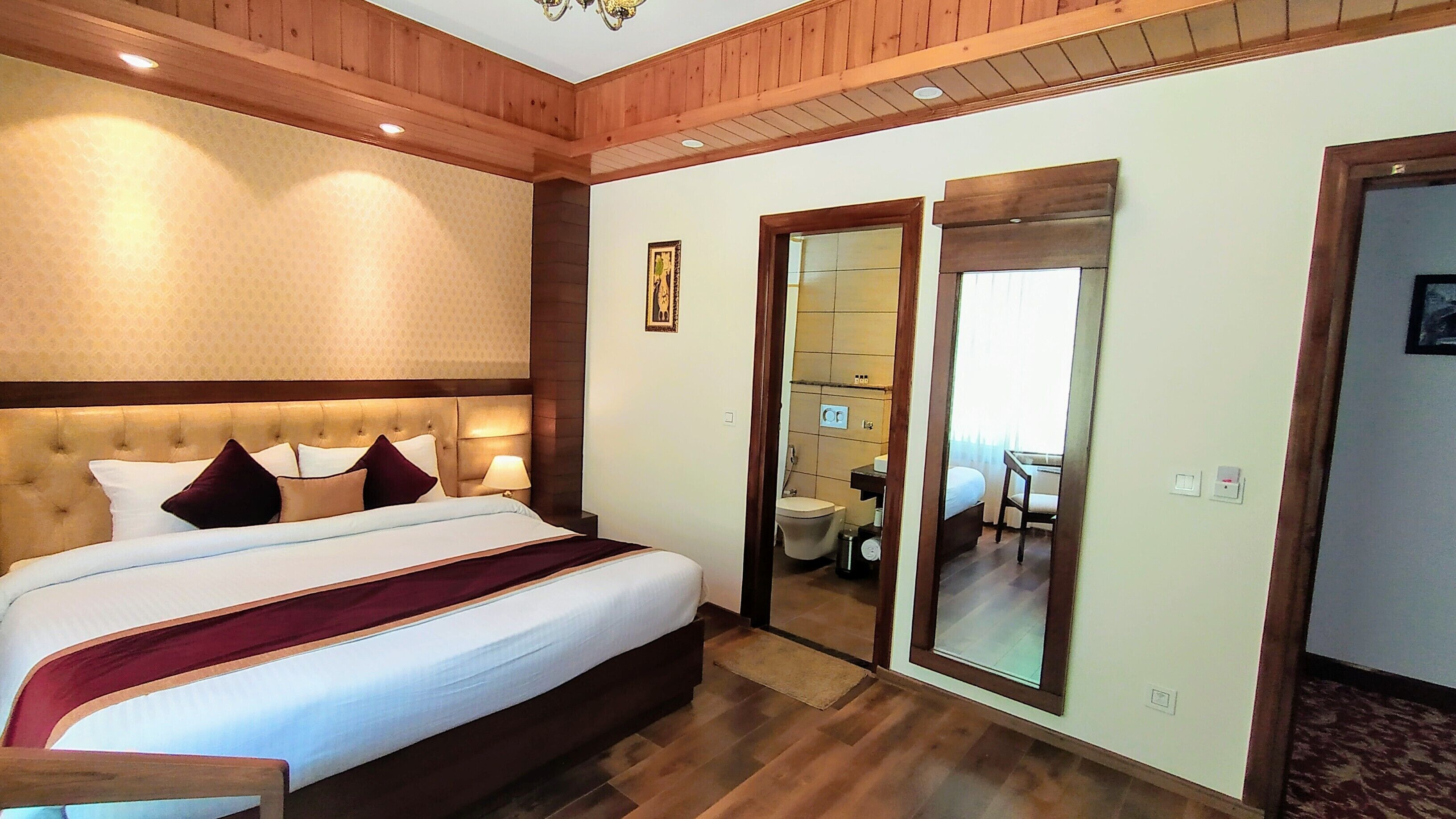 Ein Hotelzimmer mit einem großen Bett, Holzboden und einem Spiegel, der ein Badezimmer mit Toilette und Waschbecken reflektiert.