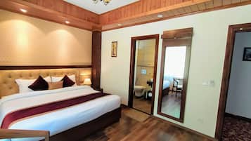 Ein Hotelzimmer mit einem großen Bett, Holzboden und einem Spiegel, der ein Badezimmer mit Toilette und Waschbecken reflektiert.