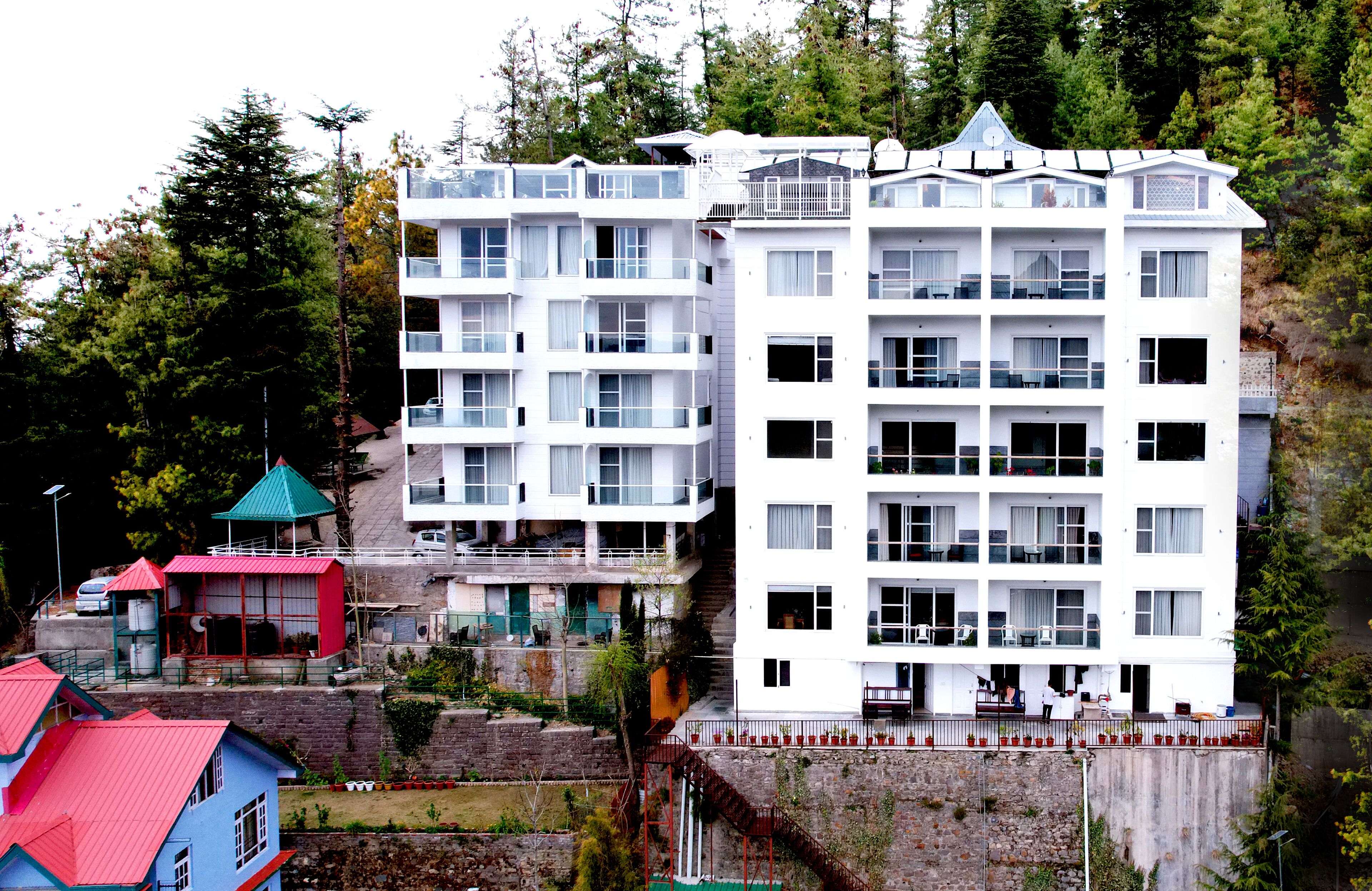 A multi-story hotel with balconies, located in a mountainous area with trees.