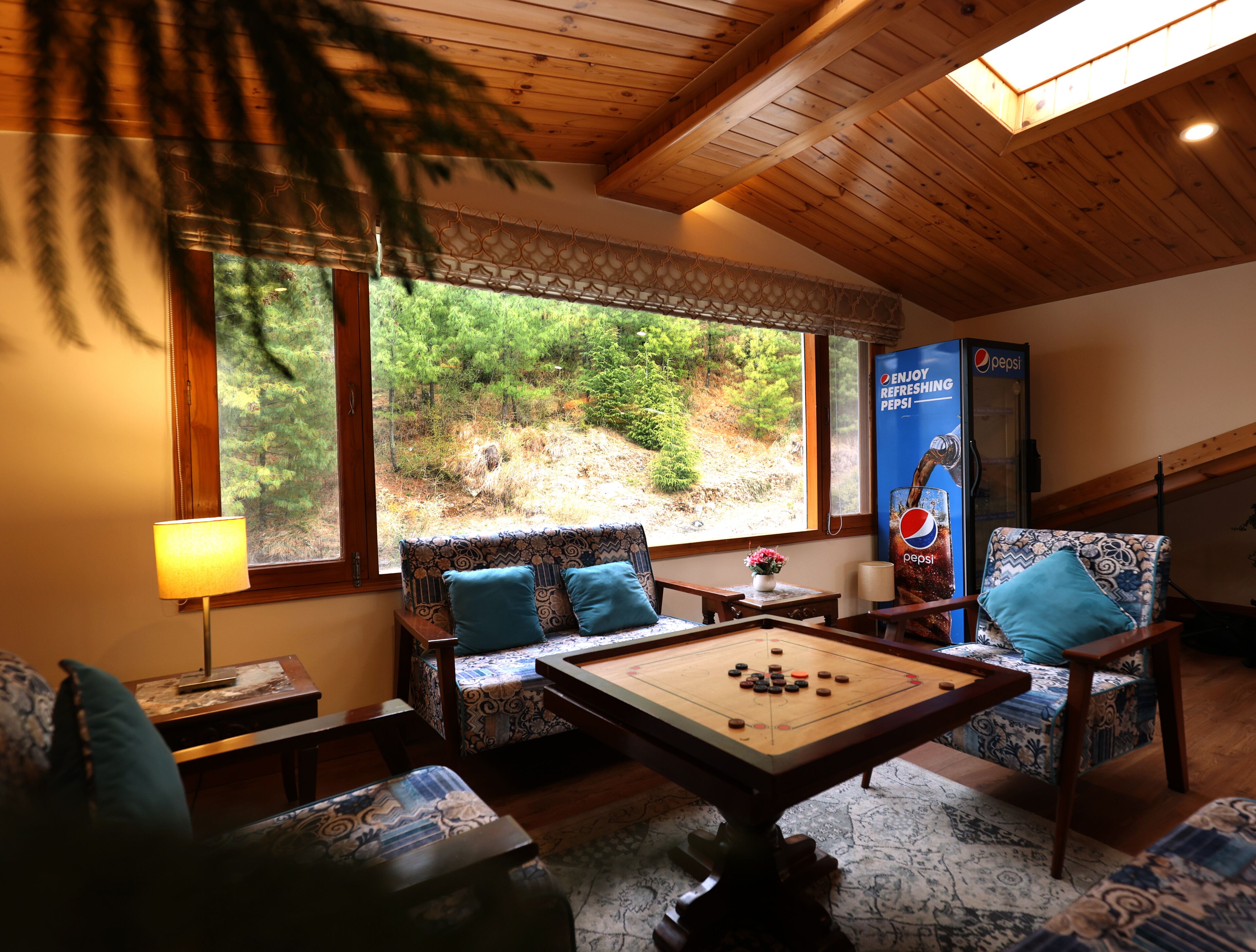 A cozy room with a pool table, comfortable seating, and a large window offering a view of a forested area.