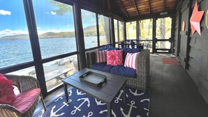 Zona relax esterna coperta con vista sul lago, arredata con mobili in vimini e decorazioni a tema nautico.