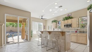 Une cuisine moderne avec un coin bar, des portes-fenêtres coulissantes donnant sur un patio et un ventilateur de plafond.
