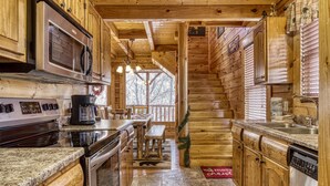 A wooden cabin kitchen with a stove, microwave, and sink. - Bear-riffic View | Hot Tub, Games & Scenic Decks (Sevierville)