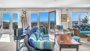 A spacious living room with a large window, a wooden table, and a blue-striped sofa. - Jonah's Whale: Large Oceanfront Home, Ocean and Waterway Views (Caswell Beach)