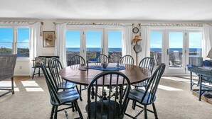 A dining area with a round table, black chairs, and a view of the ocean through large windows. - Jonah's Whale: Large Oceanfront Home, Ocean and Waterway Views (Caswell Beach)