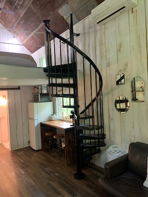 A kitchen with a wooden table and chairs, a white refrigerator, and a black spiral staircase. - Romantic Treehouse on Working Family Farm-Flower & Goats-near Chattanooga (Flintstone)