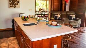 A kitchen with a large island, wooden cabinets, and a dining area with a couch and chairs. - Family Friendly Private Beach Resort, Pool, Dive Shop, Nature, Bar & Grill (Palmetto Bay)