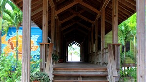 A wooden covered walkway with steps leading to a building, surrounded by greenery and a mural on the left. - Family Friendly Private Beach Resort, Pool, Dive Shop, Nature, Bar & Grill (Palmetto Bay)
