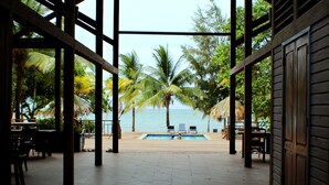 A wooden deck with a pool, palm trees, and a view of the ocean. - Family Friendly Private Beach Resort, Pool, Dive Shop, Nature, Bar & Grill (Palmetto Bay)