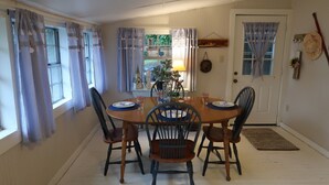 A dining room with a wooden table and four chairs, a lamp, and a window with curtains. - Lakehouse, Sleeps 6, Private Dock, Infinity Beach Pit, 2 Kayaks! (Hawkins)