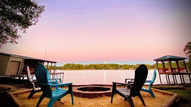 A lakeside deck with two chairs and a fire pit, overlooking a calm lake with a sunset sky. - Lakehouse, Sleeps 6, Private Dock, Infinity Beach Pit, 2 Kayaks! (Hawkins)