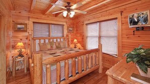 A cozy log cabin bedroom with a wooden bed, two bedside lamps, a ceiling fan, and a framed picture on the wall. - Time Well Wasted | Hot Tub, Game, Loft, Resort Pool, Views & Family-Friendly (Sevierville)