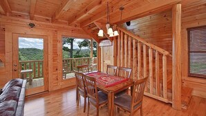 A wooden cabin interior with a dining table, chairs, and a staircase. - Time Well Wasted | Hot Tub, Game, Loft, Resort Pool, Views & Family-Friendly (Sevierville)