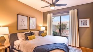 A bedroom with a large bed, two bedside lamps, a ceiling fan, and a view of a building through a window. - Jewel House West Sedona with Private Hot Tub! (Sedona)