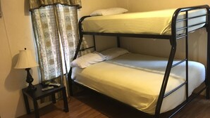 Uma cama beliche com duas almofadas, uma mesinha de cabeceira com abajur e uma cortina.