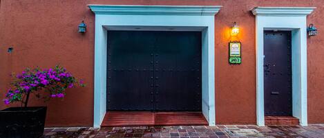 Un bâtiment avec deux portes sombres, un pot de fleurs contenant des plantes aux fleurs violettes et une entrée pavée de pierres.