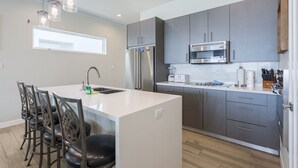 Una cocina moderna con gabinetes grises, electrodomésticos de acero inoxidable y una isla central con taburetes de bar.