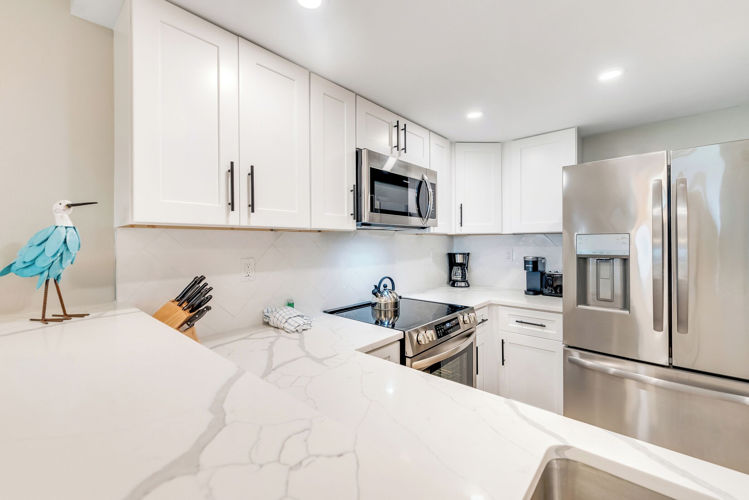 A modern kitchen with white cabinets, stainless steel appliances, and a marble countertop.