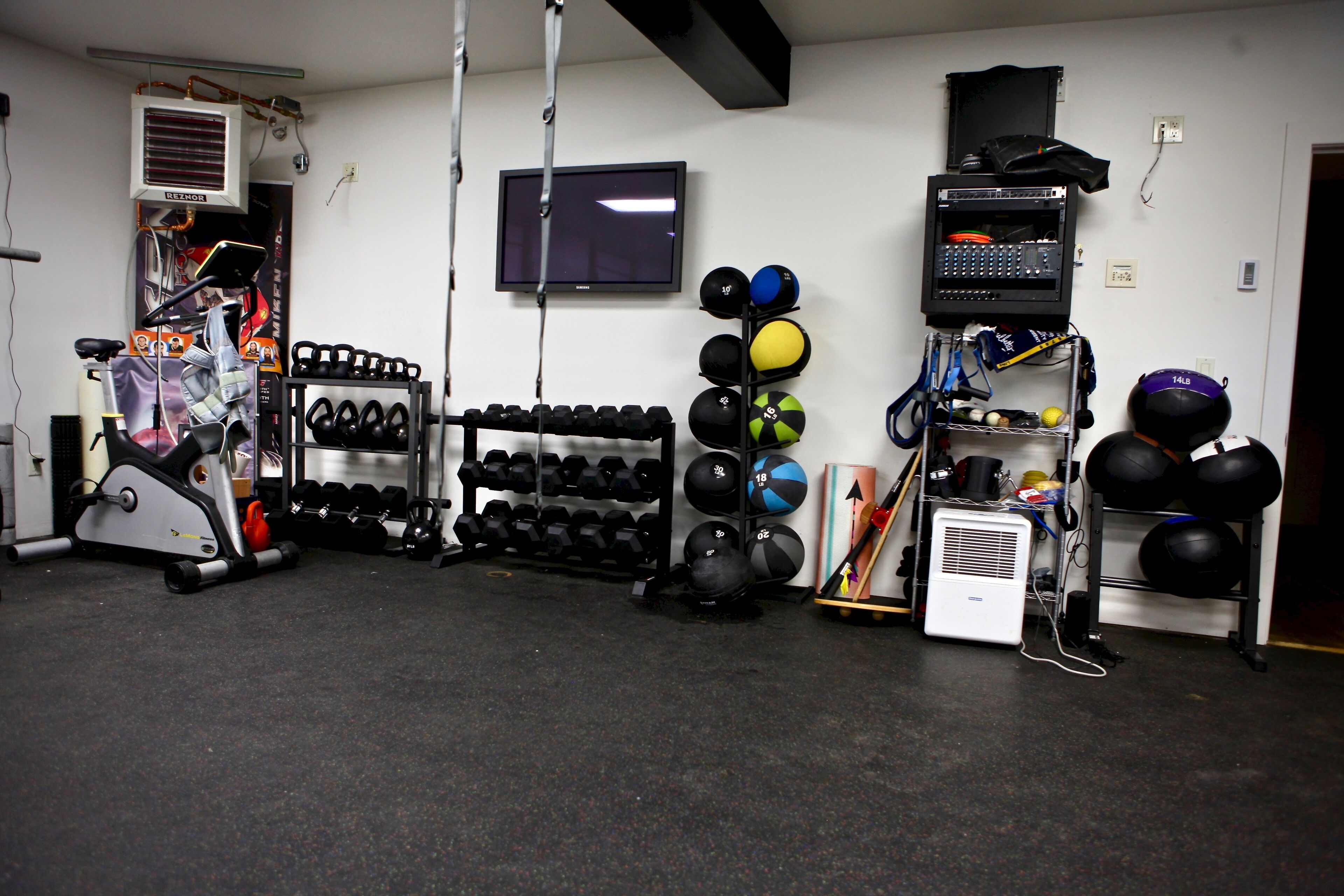 Een fitnessruimte met trainingsapparatuur, een televisie en diverse sportballen.
