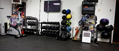 Een fitnessruimte met trainingsapparatuur, een televisie en diverse sportballen.
