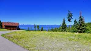 A lodge with a red roof and wooden exterior, a paved path leading to it, and a view of mountains and a lake.