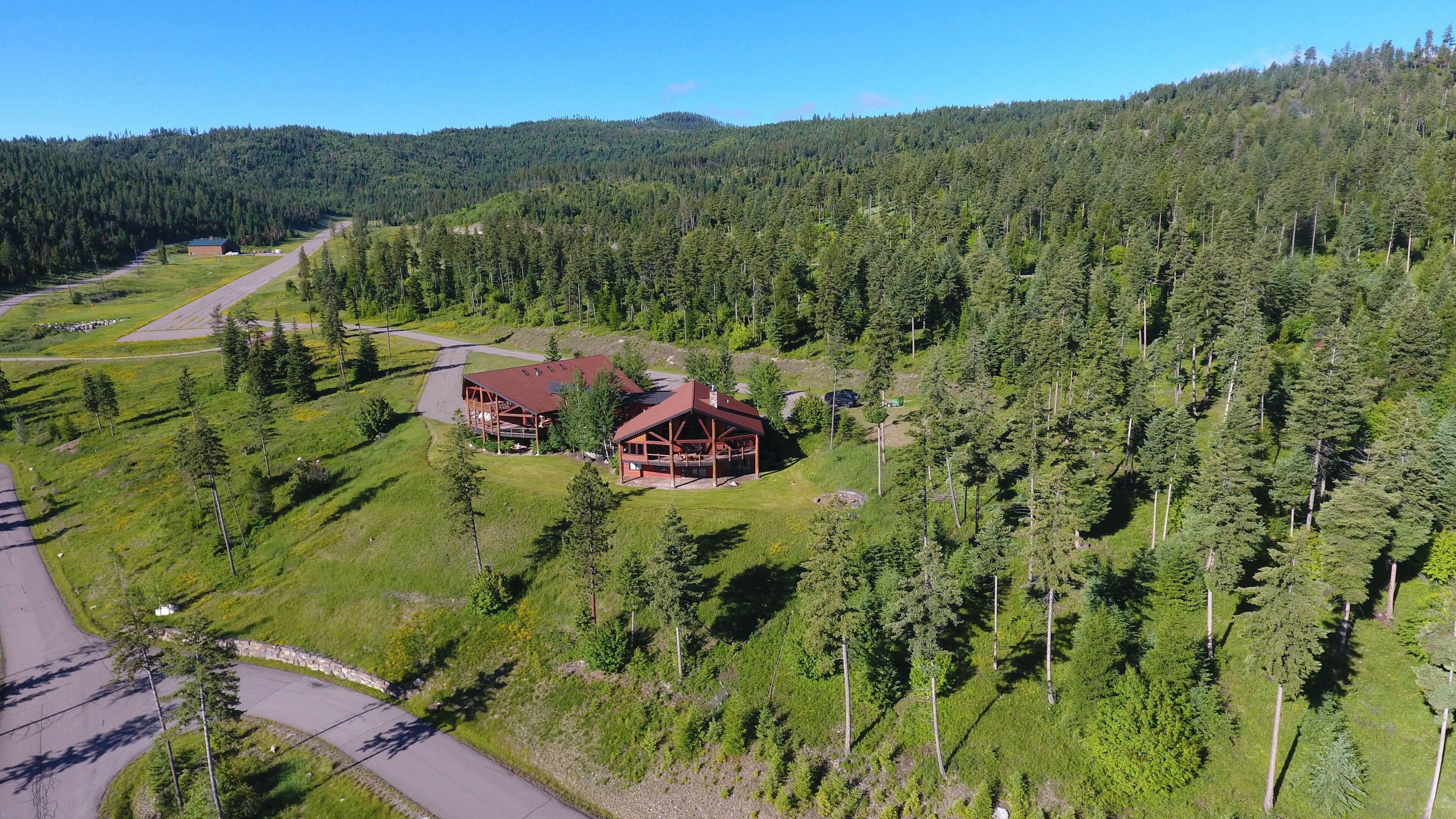 A lodge with a red roof, surrounded by dense forest and a clear sky.