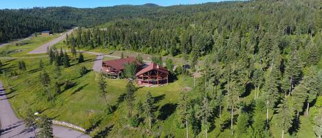 A lodge with a red roof, surrounded by dense forest and a clear sky.