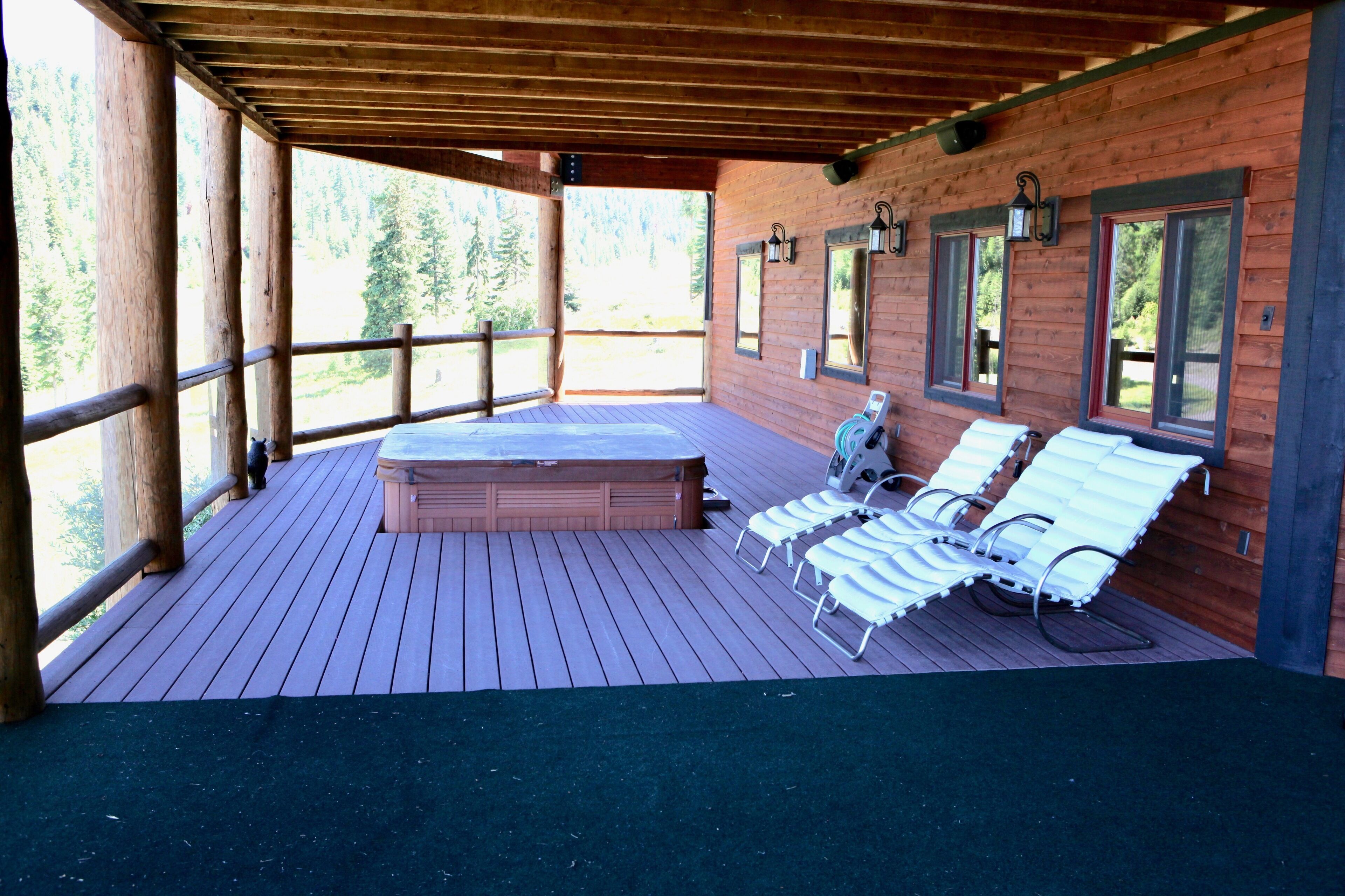Eine Holzterrasse mit Whirlpool, Liegestühlen und einem Holzhäuschen.