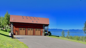 A red building with a garage, a stone pillar, and a view of mountains and a lake.
