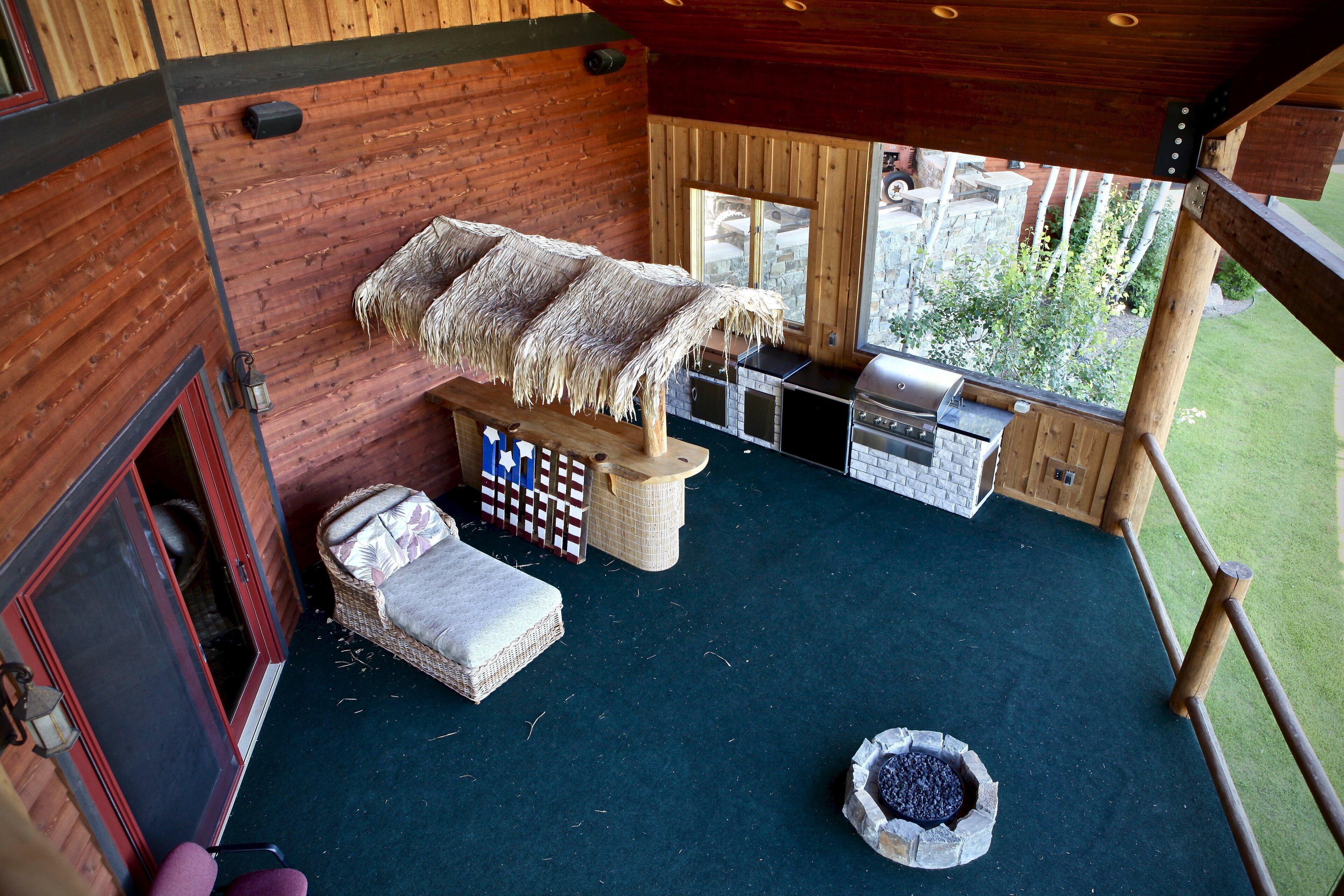 A cozy cabin with a thatched roof, a fireplace, a grill, and a view of the surrounding greenery.