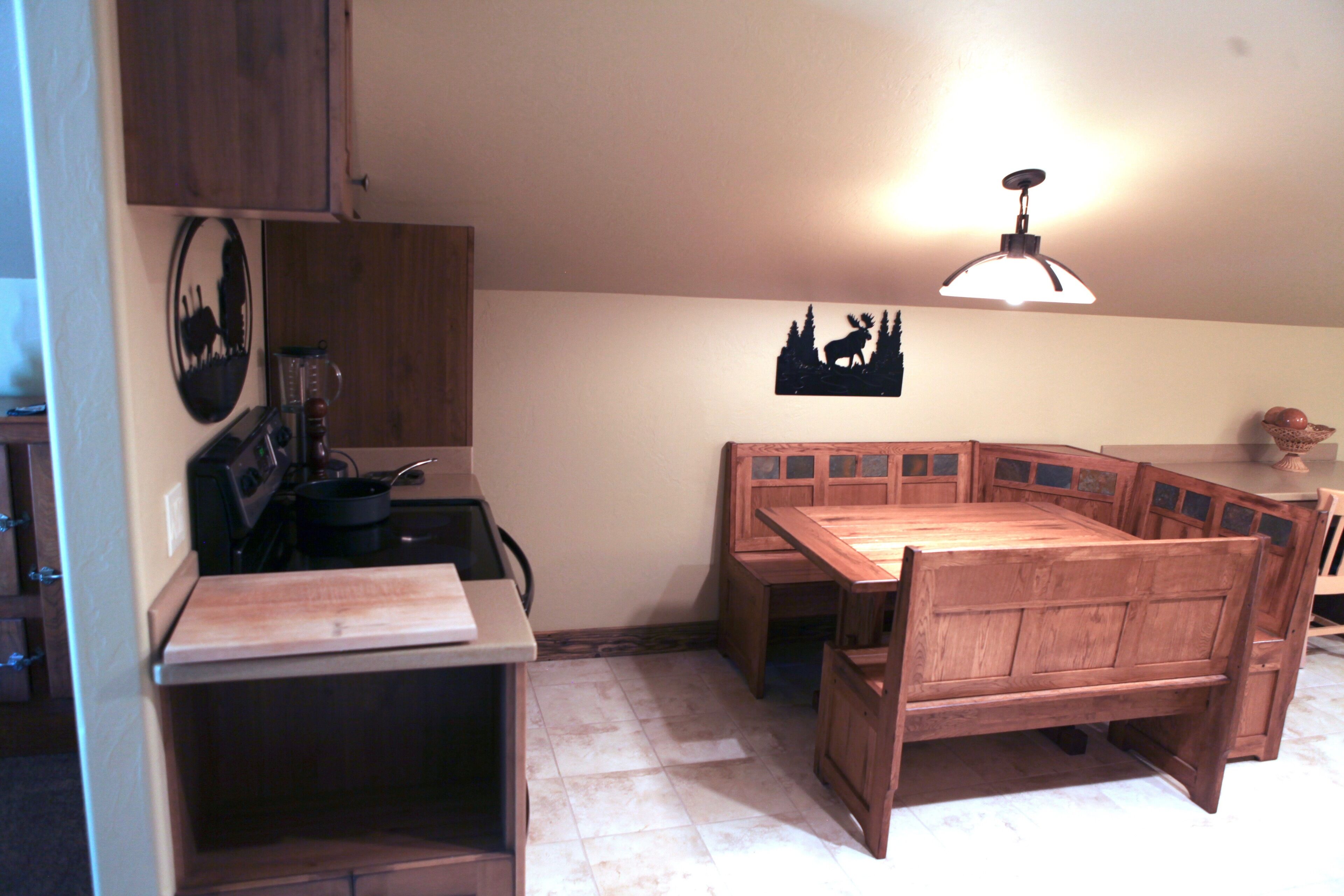 A compact kitchen with a wooden table and bench, a stove, and a wall-mounted light fixture.