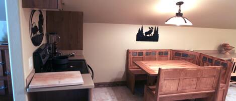 A compact kitchen with a wooden table and bench, a stove, and a wall-mounted light fixture.